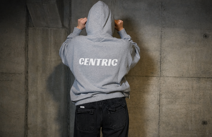 Person wearing a gray hoodie with 'CENTRIC' printed on the back against a concrete wall.